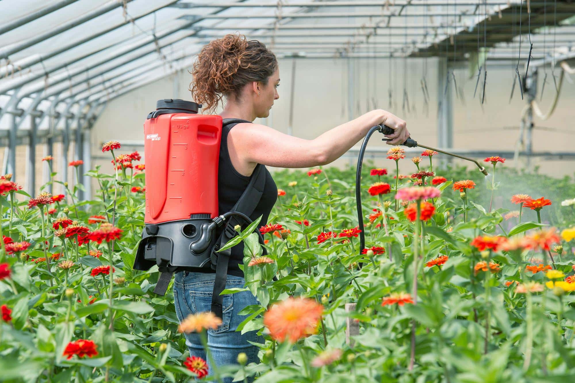 Vrouw behandelt bloeiende planten met een rugspuit in een serre